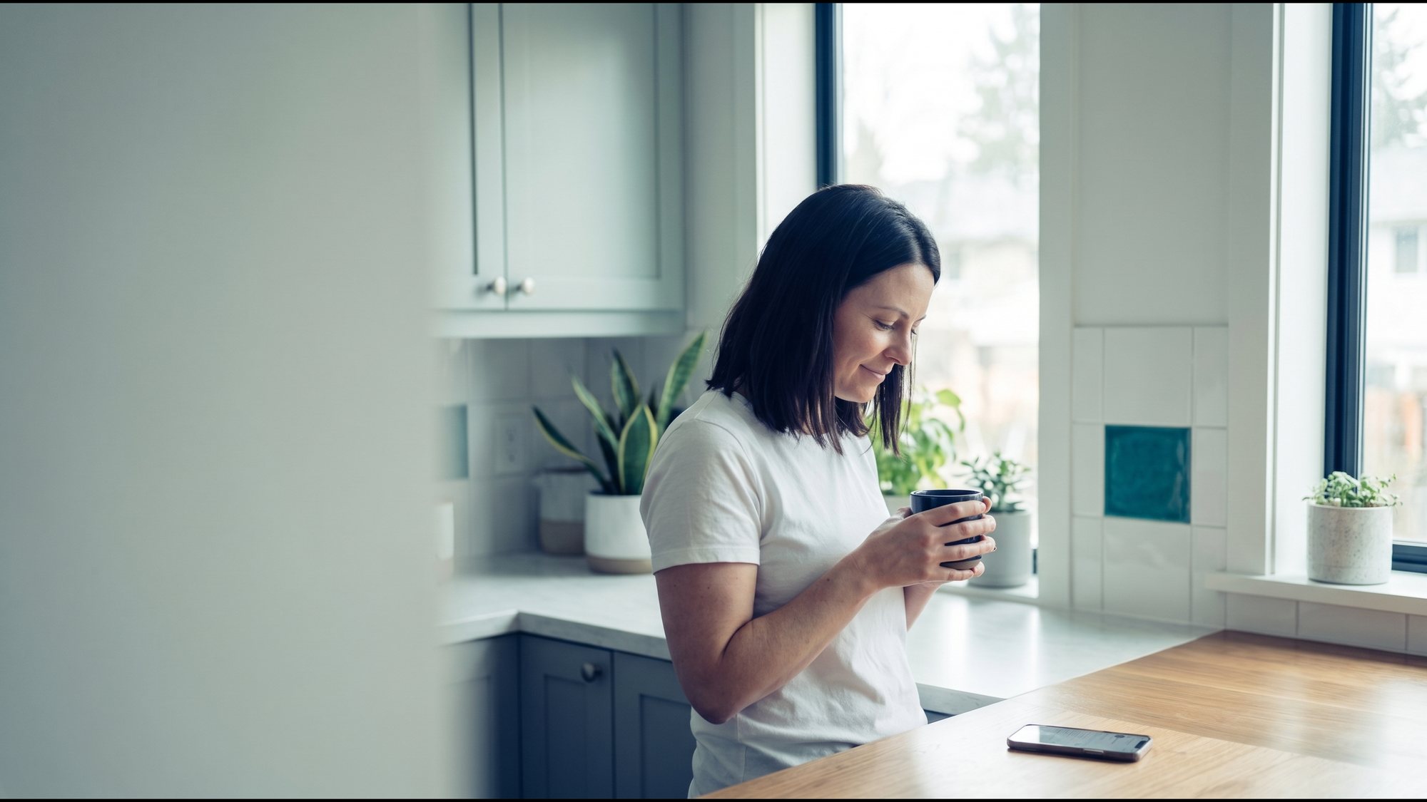 The same woman at a bright kitchen window in the morning, holding a mug.